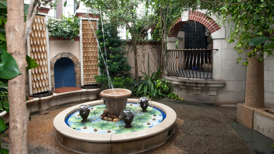 a small fountain in the middle with building structures and green trees surrounding it