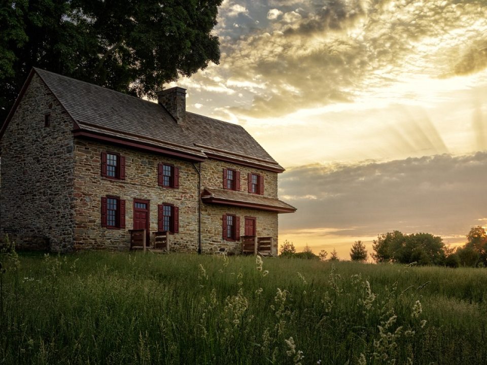 a stone farmhouse with red shutters and a large tree behind it 