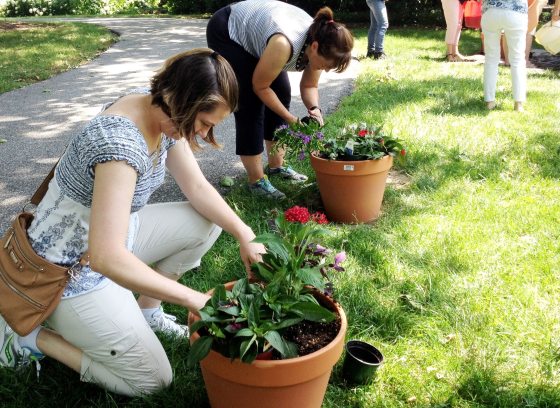 Two woman plant flowers in terra cotta containers.