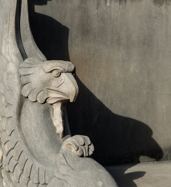 The end of a stone bench with a carved head of an eagle in it.