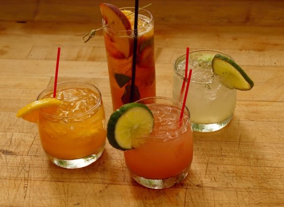 Four cocktails in glasses on a wooden table.