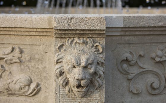A stone decorative carved lion head adorns a stone fountain structure