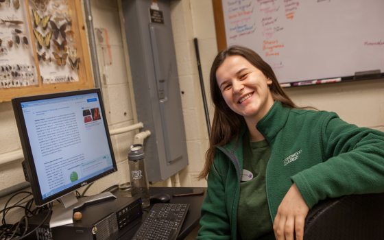 a student sitting in front of a computer turns to smile at the camera