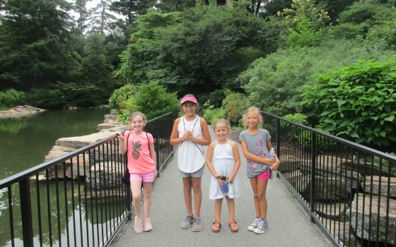 Four young people standing on a paved bridge smiling at the camera.