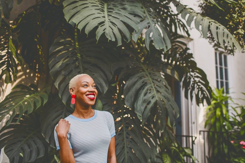A woman stands looking to the side in front of a large green monstera plant