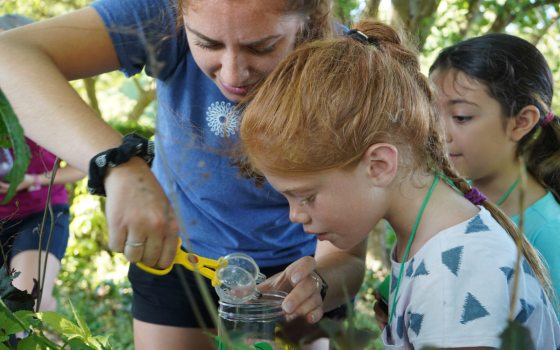 Two students and a teacher examining a plant with a magnifying glass.
