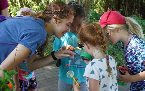 Three children and an educator hundling in a circle examining a plant.