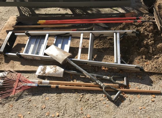 Shovels and a ladder laying on the dirt ground.