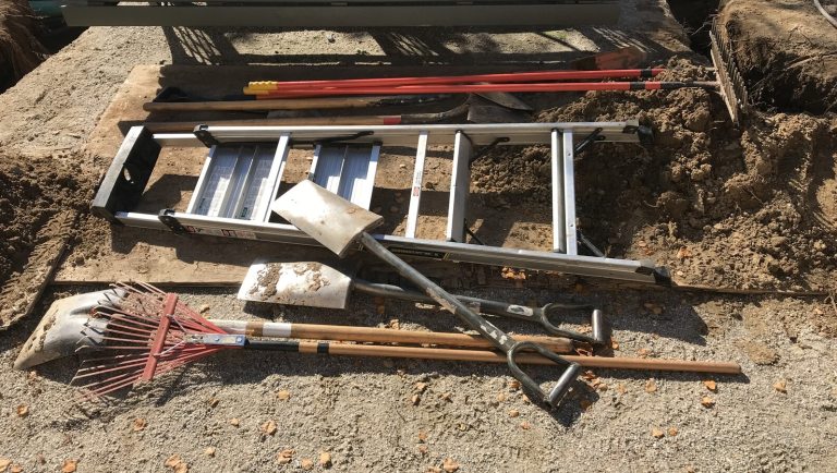Shovels and a ladder laying on the dirt ground.