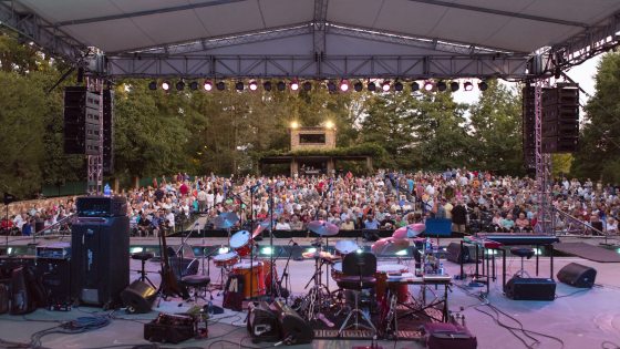 a stage is full of instruments before a concert with a full crowd waiting in their seats in the distance