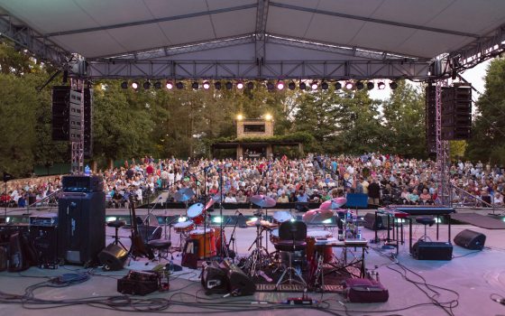 a stage is full of instruments before a concert with a full crowd waiting in their seats in the distance