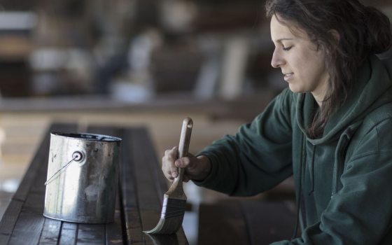 a person in a dark green sweatshirt applies a paintbrush to a dark wood surface