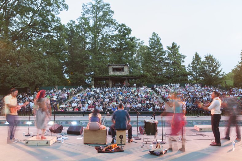 a view behind singers and dancers on a stage with a crowd of people in the background 