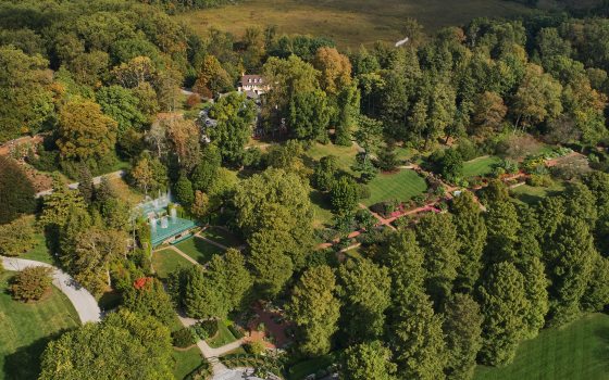 Aerial view of house and theater gardens filled with trees, a small fountain garden, and brick house