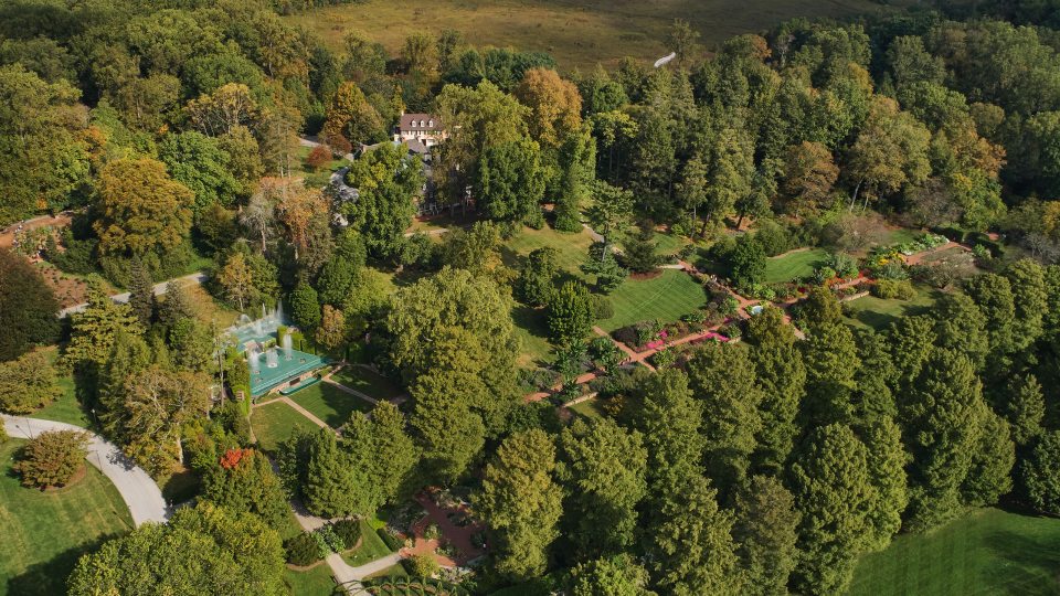 Aerial view of house and theater gardens filled with trees, a small fountain garden, and brick house