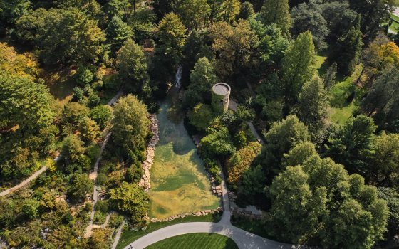 Aerial view of large grassy area with a small pond and stone tower surrounded by a forest