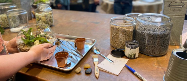 a set of hands holding a terrarium with a group of people talking in the background 