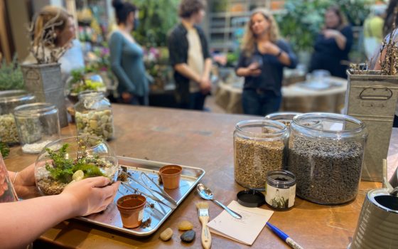 a set of hands holding a terrarium with a group of people talking in the background 