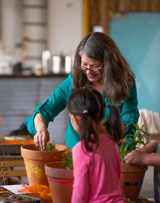 three people planting a a plant in a painted terra cotta pot