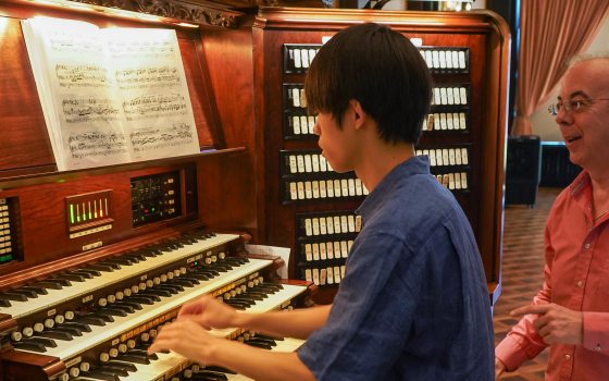 an instructor stands next to a student at the organ console