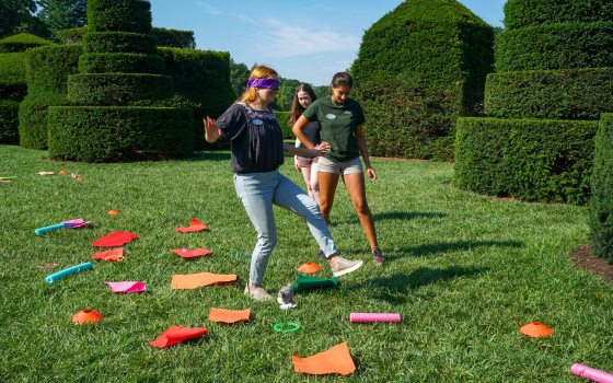 Three students in a topiary garden playing a game with colorful stones. 