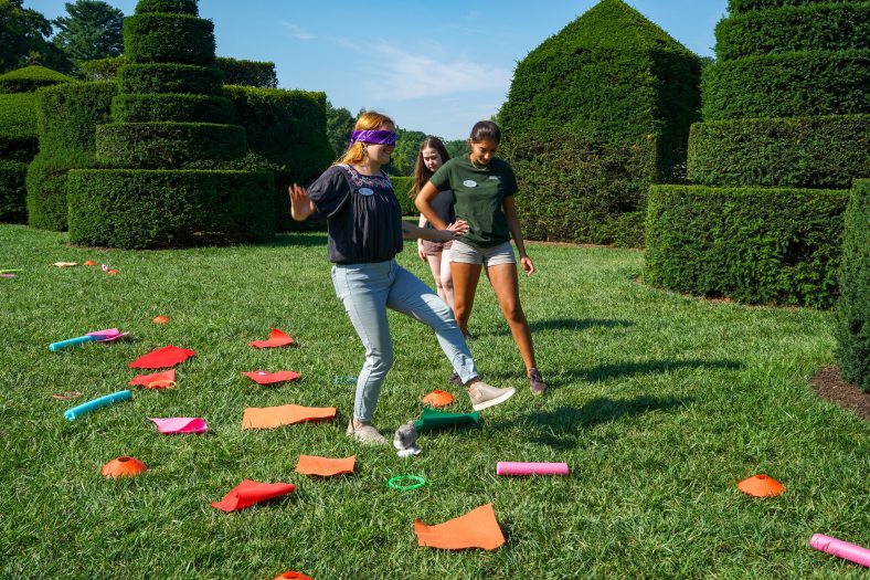 Three students in a topiary garden playing a game with colorful stones. 