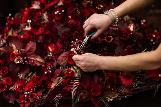 a person with pliers near a floral bouquet of red and gold flowers and leaves