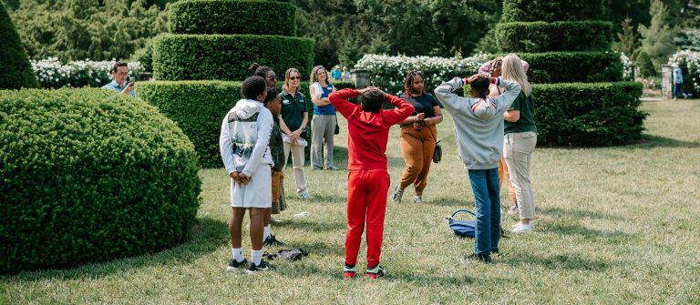 A group of students standing in a circle in a topiary garden.