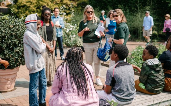 A group of students listening to an educator in an outdoor garden.