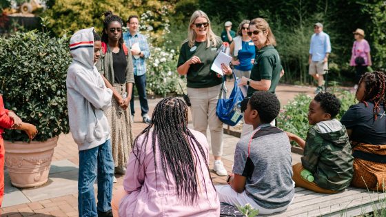 A group of students listening to an educator in an outdoor garden.