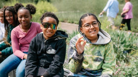 Students stitting on a stone wall in a garden smiling at the camera.