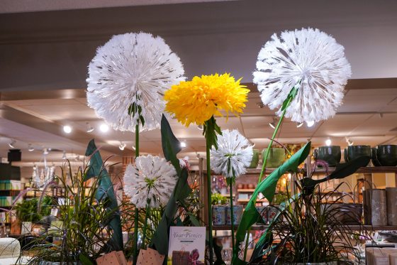 Large handmade paper flowers in yellow and white hanging in a gift shop.