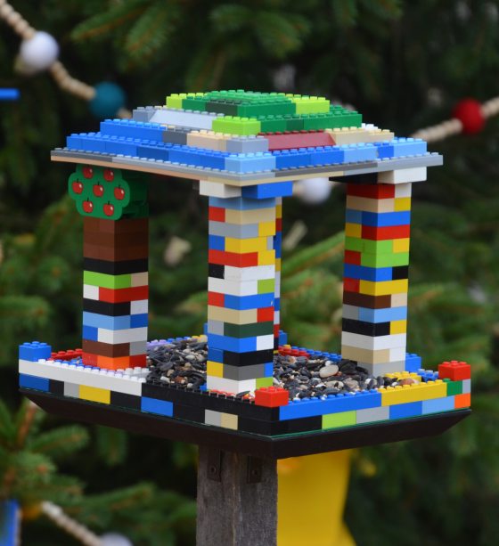 A birdhouse made from lego blocks hanging on an outdoor evergreen tree.