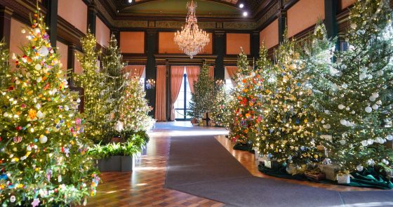 A large ballroom filled with decorated Christmas trees. 