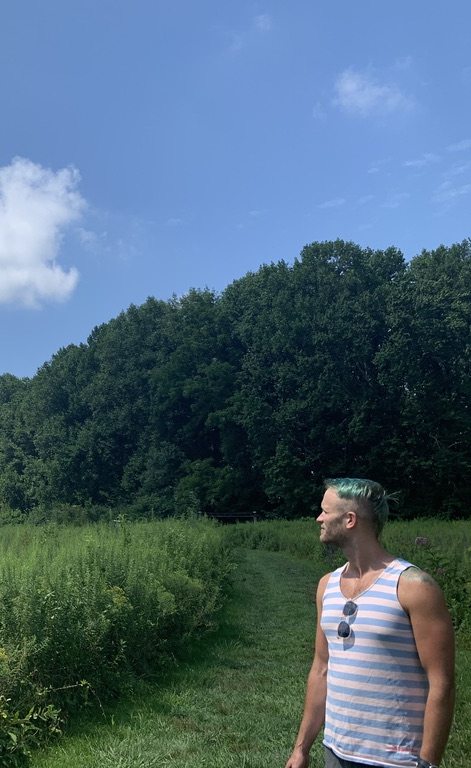 a person outdoor on a green grass trail overlooking a meadow