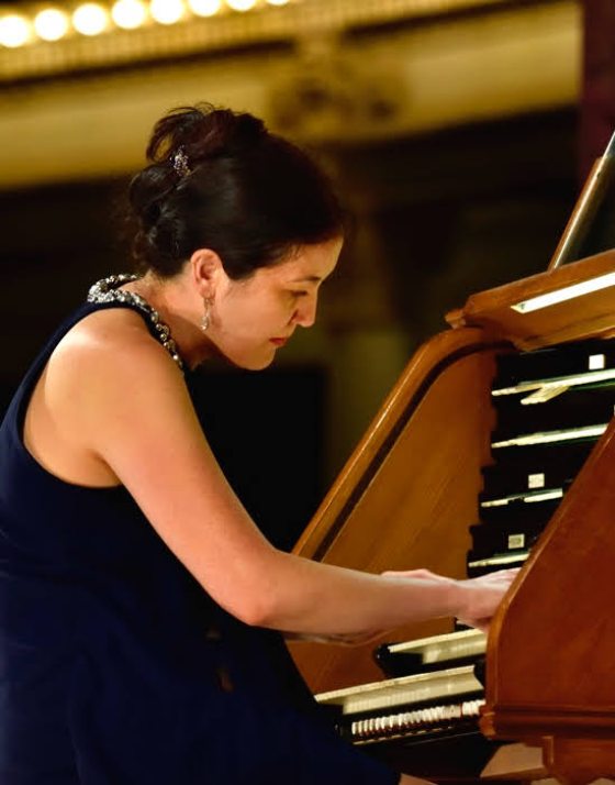 A person in a black dress seated intently, playing an organ. 