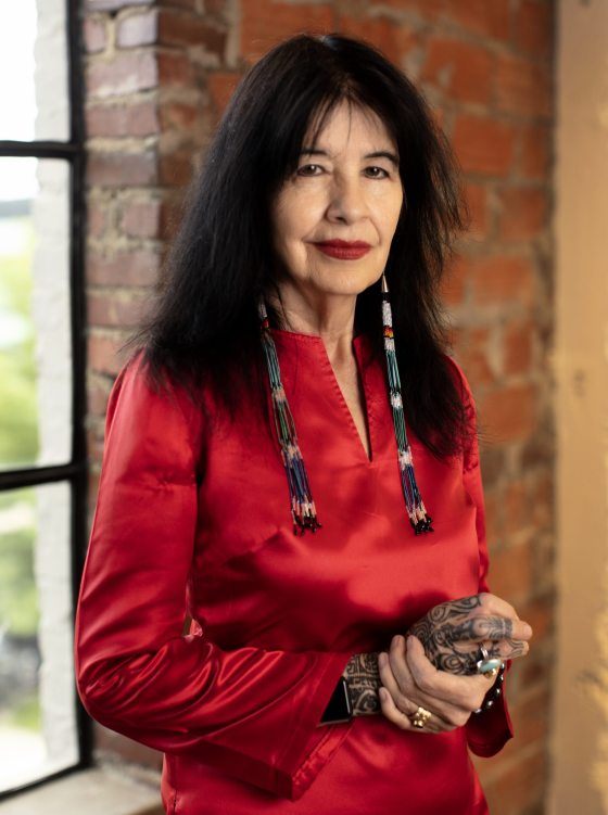 Woman standing, facing the camera, in red satin shirt and long beaded earrings