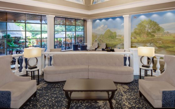 A view of a hotel lobby with three white sofas and large windows.