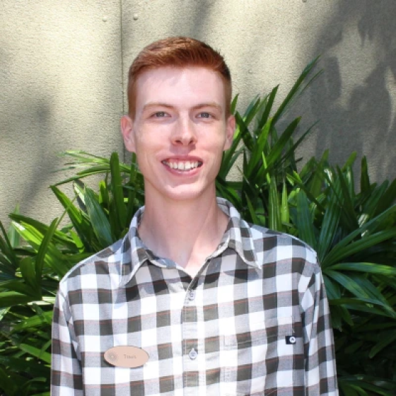 Portrait of person with very short reddish-brown hair and broad smile, wearing a black and white checkered shirt.